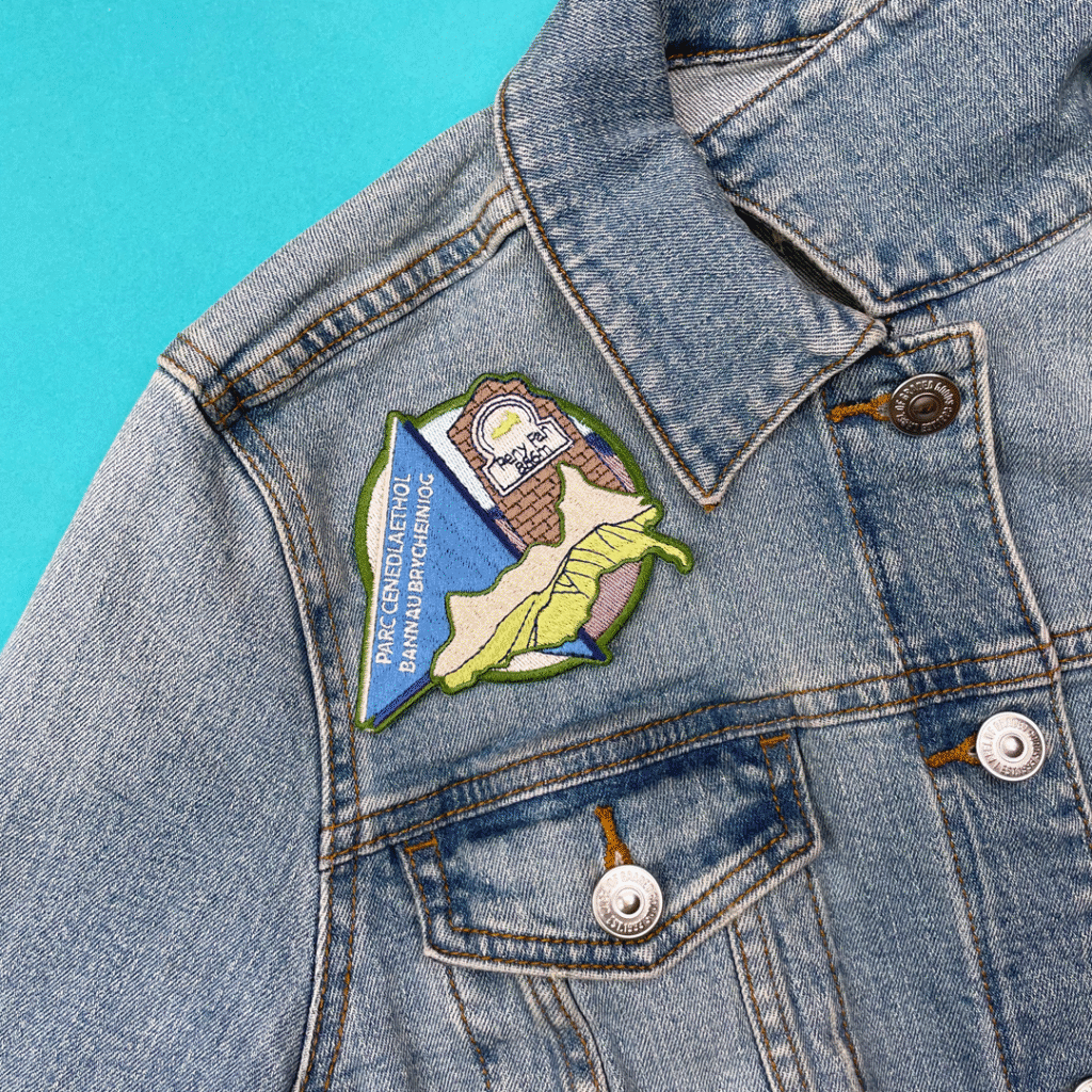 Denim jacket with colorful map patch and “PARQUE DE ANCHO BANANA BEACH LOC” above chest pocket.
