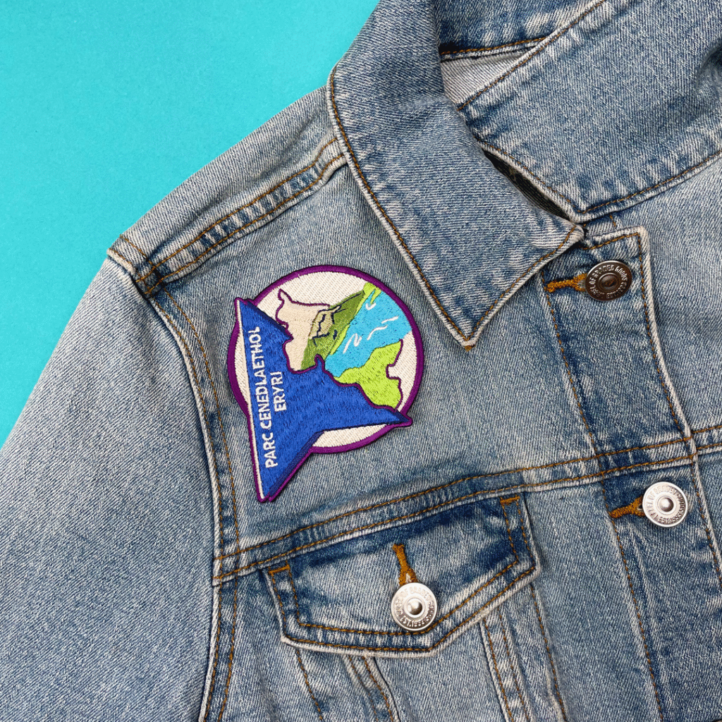Denim jacket with a colorful map patch, mountains, rivers, and PARC CENDAI ETNOL ENRY text.