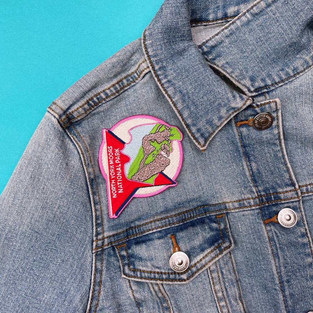Denim jacket with chest patch: green dinosaur, pink star, NORTH FORK ROCKS NATIONAL PARK.