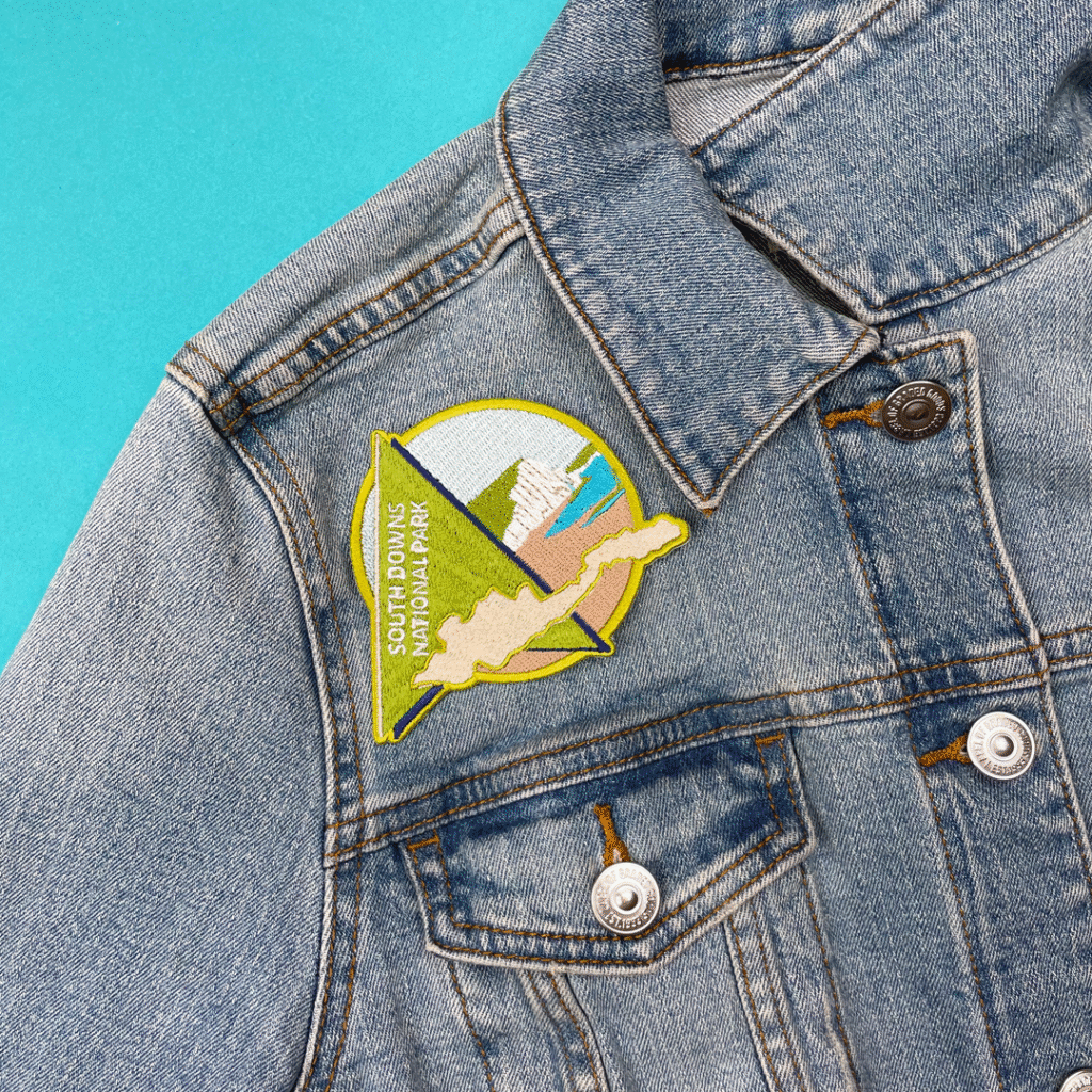 Denim jacket with South Downs National Park embroidered patch, stylized landscape, blue background.