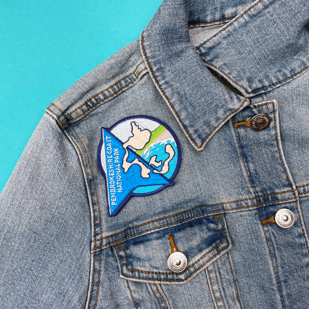 Denim jacket with colorful “PEMBROKESHIRE COAST NATIONAL PARK” map patch on light blue.