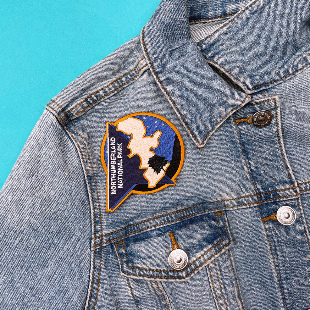 Blue denim jacket with colorful NORTHUMBERLAND NATIONAL PARK embroidered patch on chest.