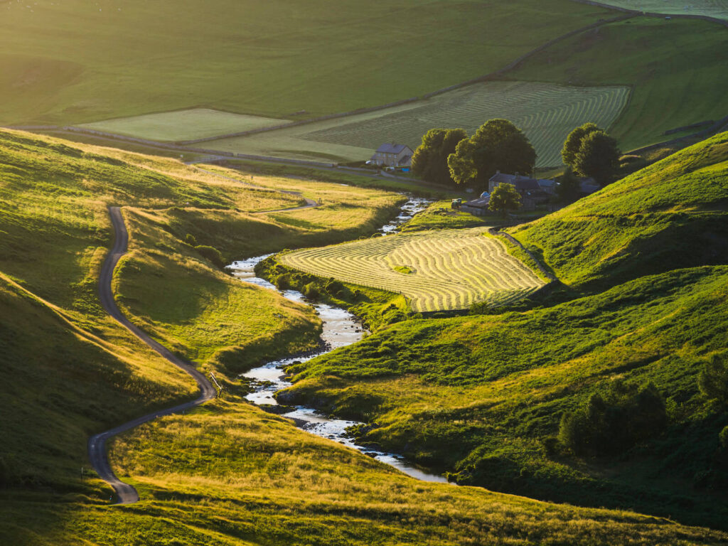 A winding path weaves through lush hills to a farmhouse, fields forming natures masterpiece.