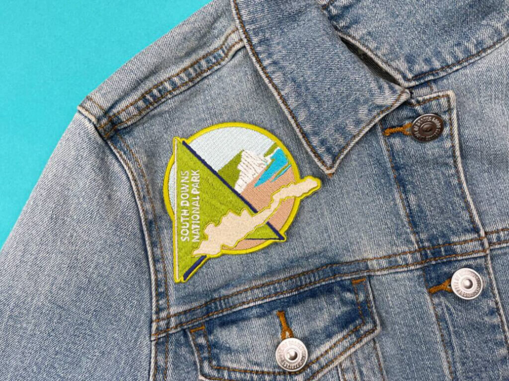 Denim jacket with a vibrant patch of South Downs, showcasing National Parks on a teal backdrop.