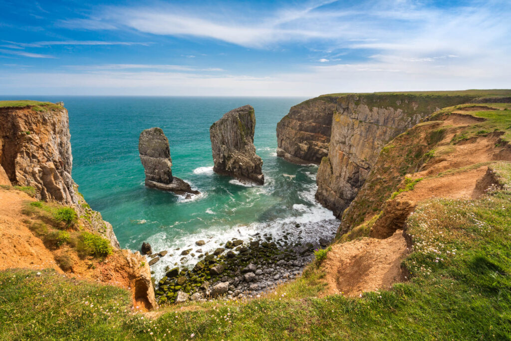 Rugged coastal cliffs rise above turquoise waves crashing on rocks—natures breathtaking beauty.