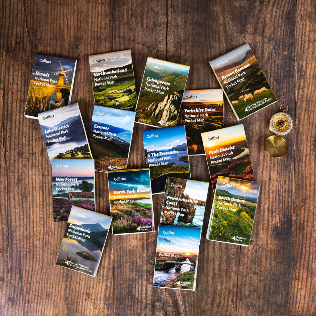 13 Collins national park pocket maps in a circle, with a compass and tea on the right side.